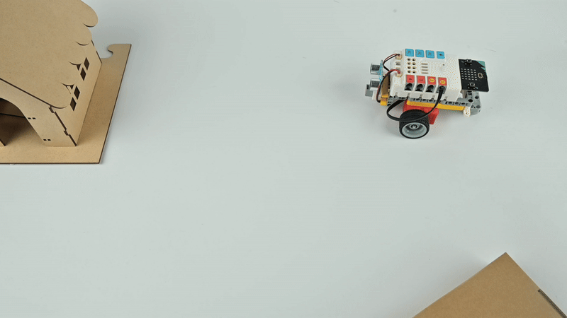 STEM robotics kit small wheeled robot moving toward cardboard house during coding project experiment