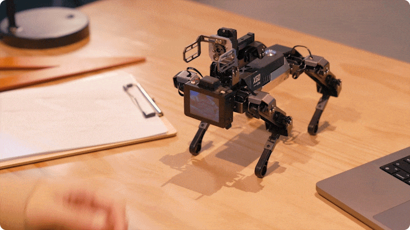 Quadruped robot dog with mechanical arm and display demonstrating movement on a desk, showcasing robotics and STEM education features